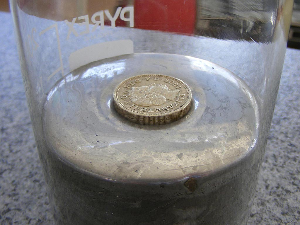 Metal coin floating on the liquid mercury surface